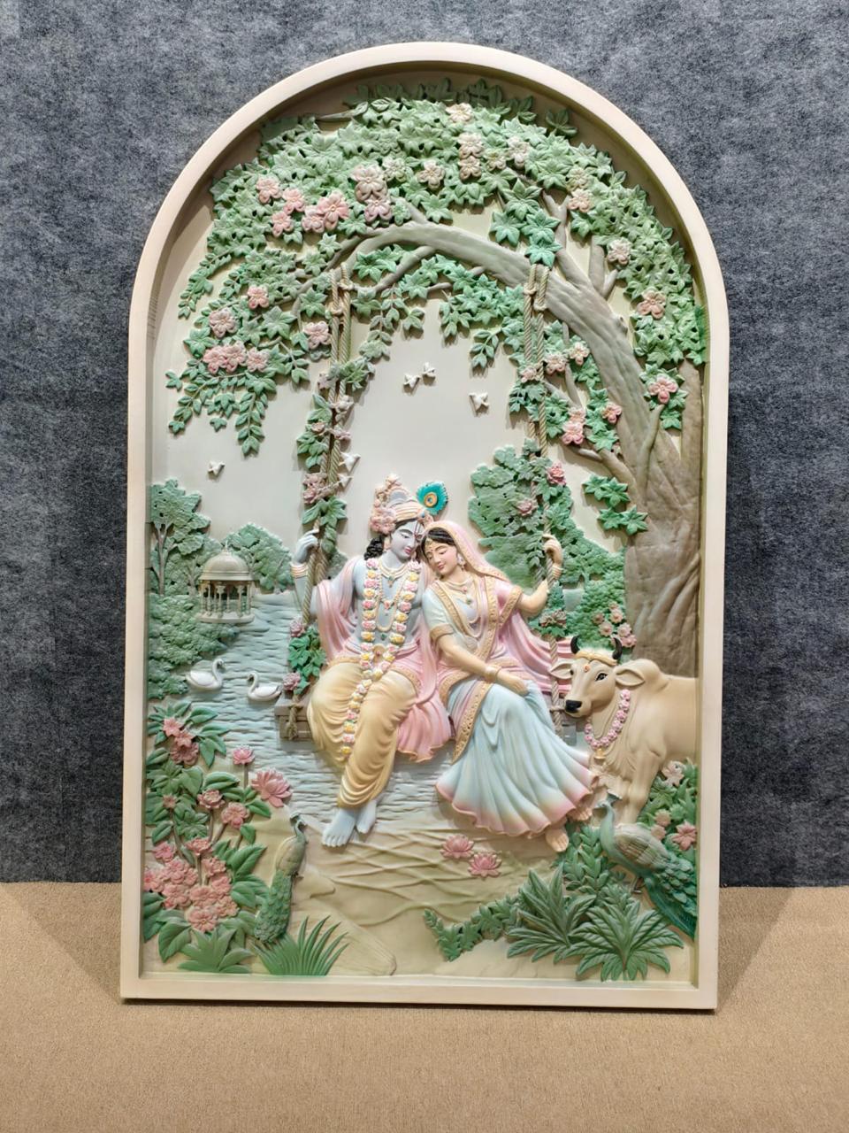 Arched carved relief of Radha and Krishna on a swing under a flowering tree, painted in soft greens and pinks