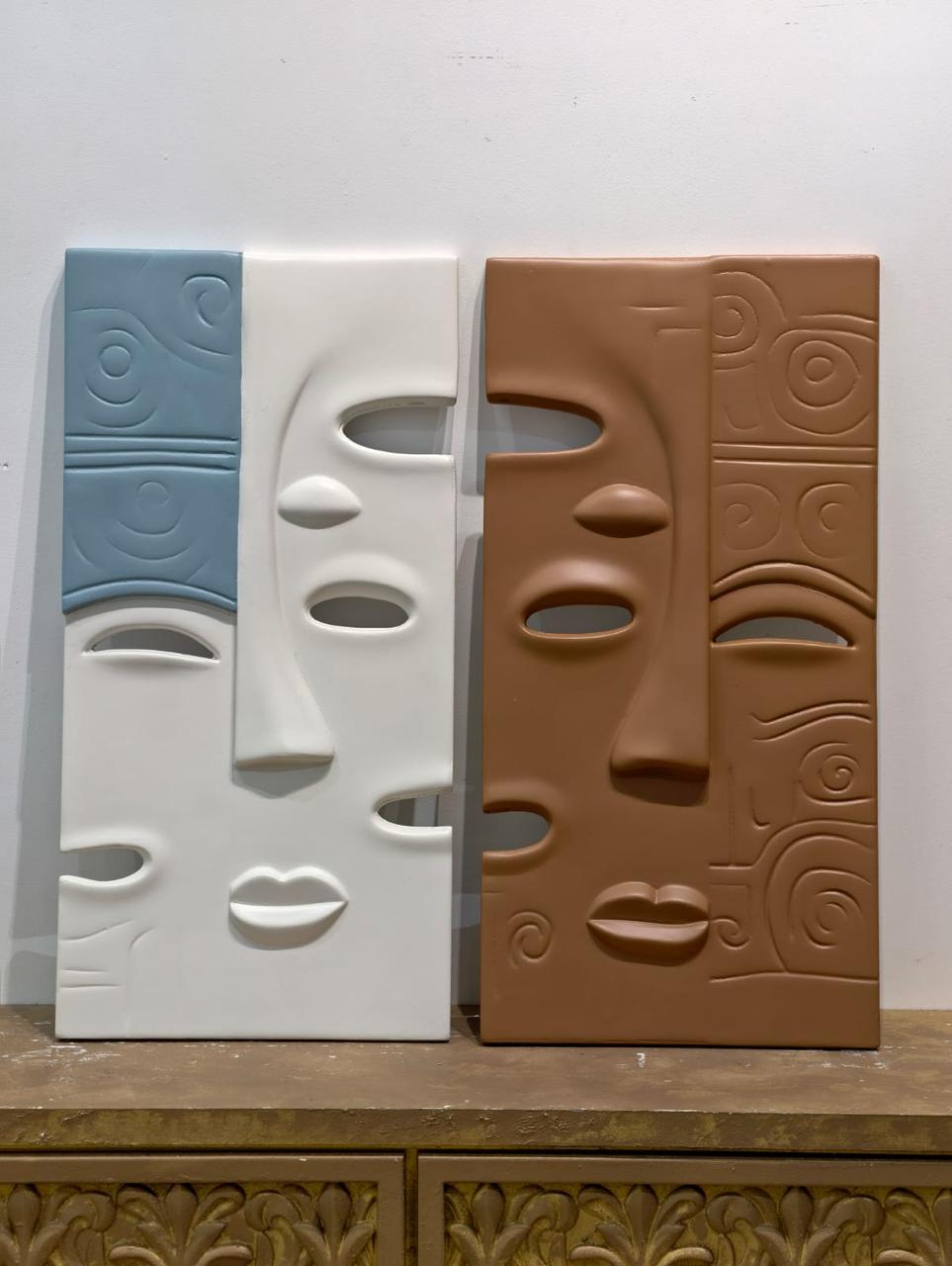 Two carved panels of stylised faces, one white and blue, one terracotta